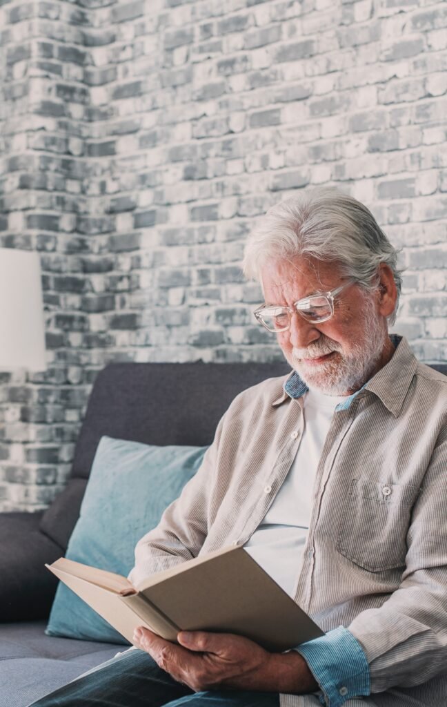 Headshot portrait close up of old happy and relaxed man sitting reading a book at home